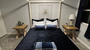 Un dormitorio con una cama, dos mesitas de noche, una lámpara, una obra de arte en la pared y una luz de techo.