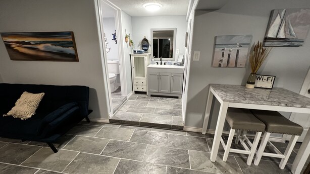Una sala de estar moderna con un sofá azul oscuro, una cocina con armarios blancos y un comedor con encimera de mármol.
