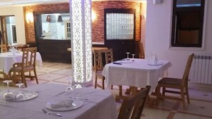 A restaurant with tables set for dining, featuring a central decorative pillar and a view of the kitchen area. - Hotel Salsabil Naoui (Djelfa)