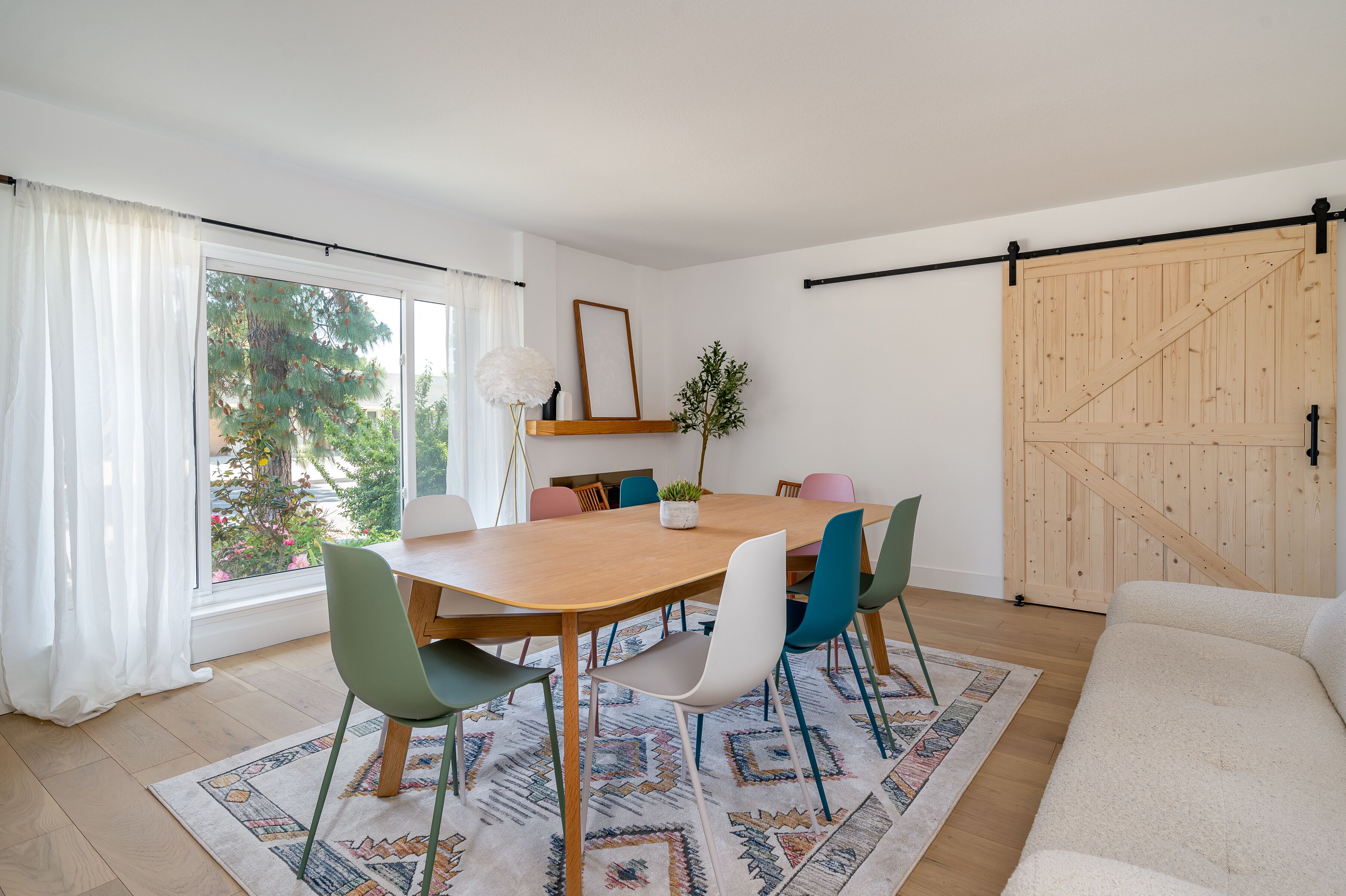 A dining area with a wooden table, colorful chairs, and a patterned rug.