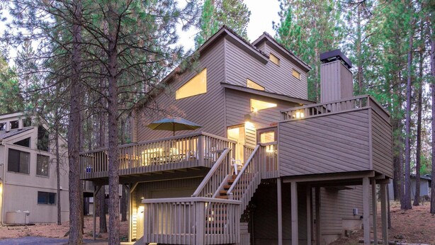 A multi-level cabin with a deck and stairs, surrounded by trees.