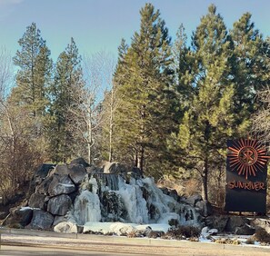 A waterfall with a sign reading "SUNRIVER" in a forested area.