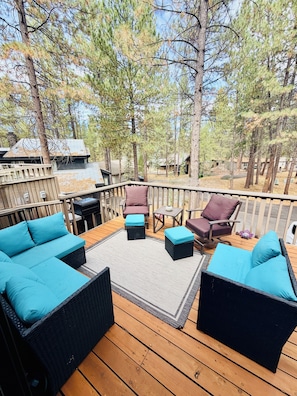 A deck with outdoor furniture, including sofas and chairs, surrounded by trees.