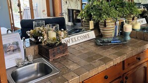 A kitchen with a stone countertop, wooden cabinets, a welcome sign, and a potted plant.