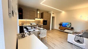 A modern kitchen with white cabinetry, a dining area with white chairs, and a living room with a TV and a sofa. - Cozy and bright apartment with a garden: pets allowed (Lombardia)