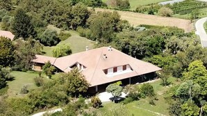 A large house with a sloped roof, surrounded by dense greenery and a vineyard in the background. - Cozy and bright apartment with a garden: pets allowed (Lombardia)