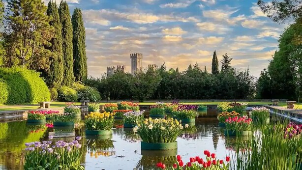 A garden with a pond, various flowers, and a distant castle-like structure. - Cozy and bright apartment with a garden: pets allowed (Lombardia)