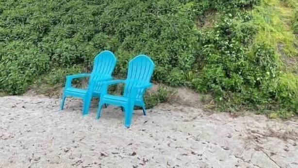 Une plage avec deux chaises bleues et une maison dotée d’un porche.
