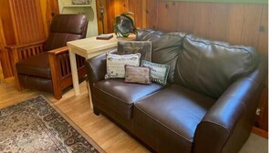 Un salon chaleureux avec un canapé en cuir marron, une table basse en bois, une lampe et des coussins décoratifs.