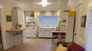 Un espacio habitable compacto con kitchenette, zona de comedor y área de estar con sofá verde y reposapiés rojo.