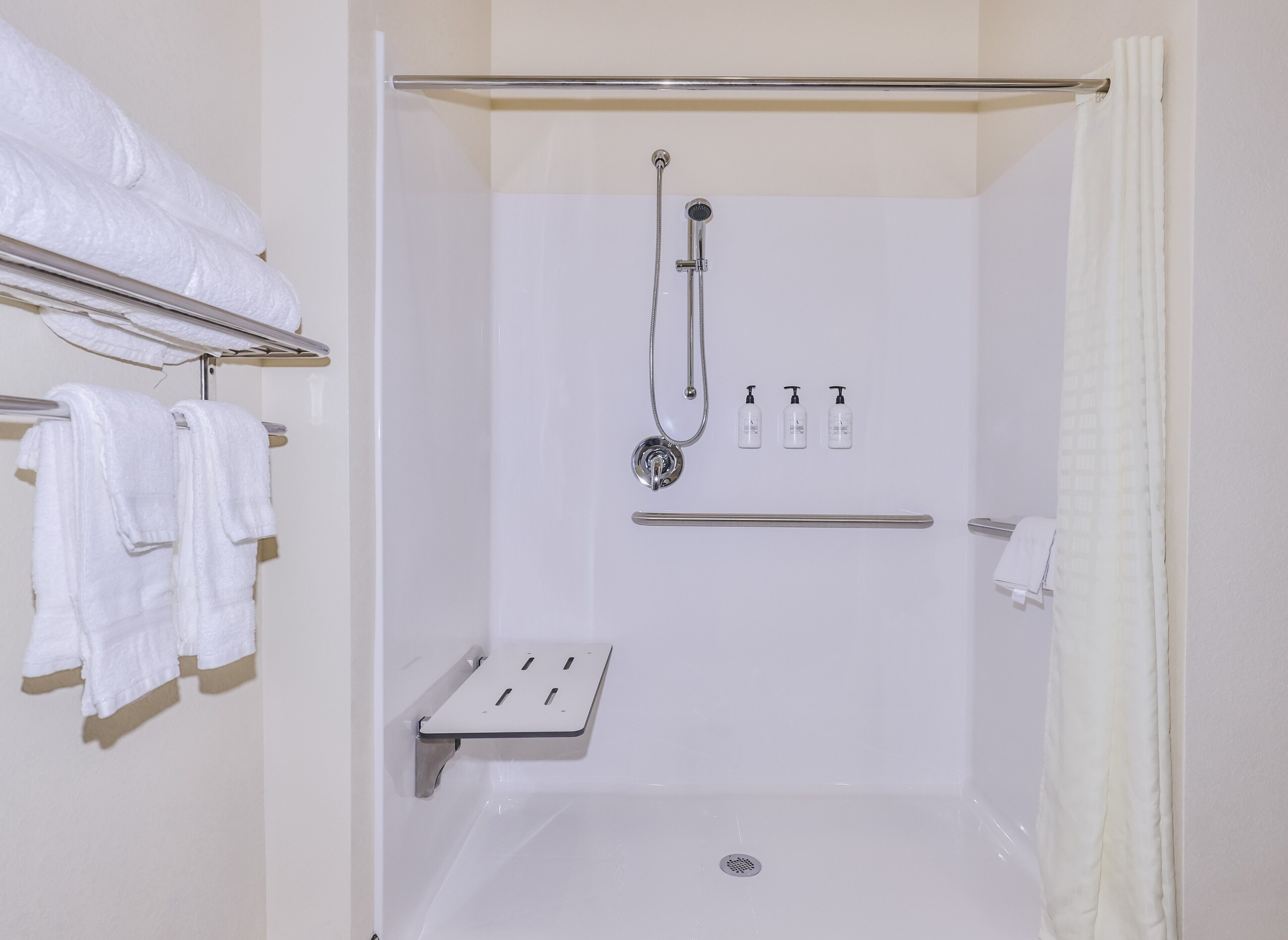 A modern bathroom with a shower, a towel rack, and a soap dispenser.