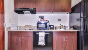 Una cocina compacta con muebles de madera oscura, una campana extractora de acero inoxidable, un microondas y un refrigerador negro.