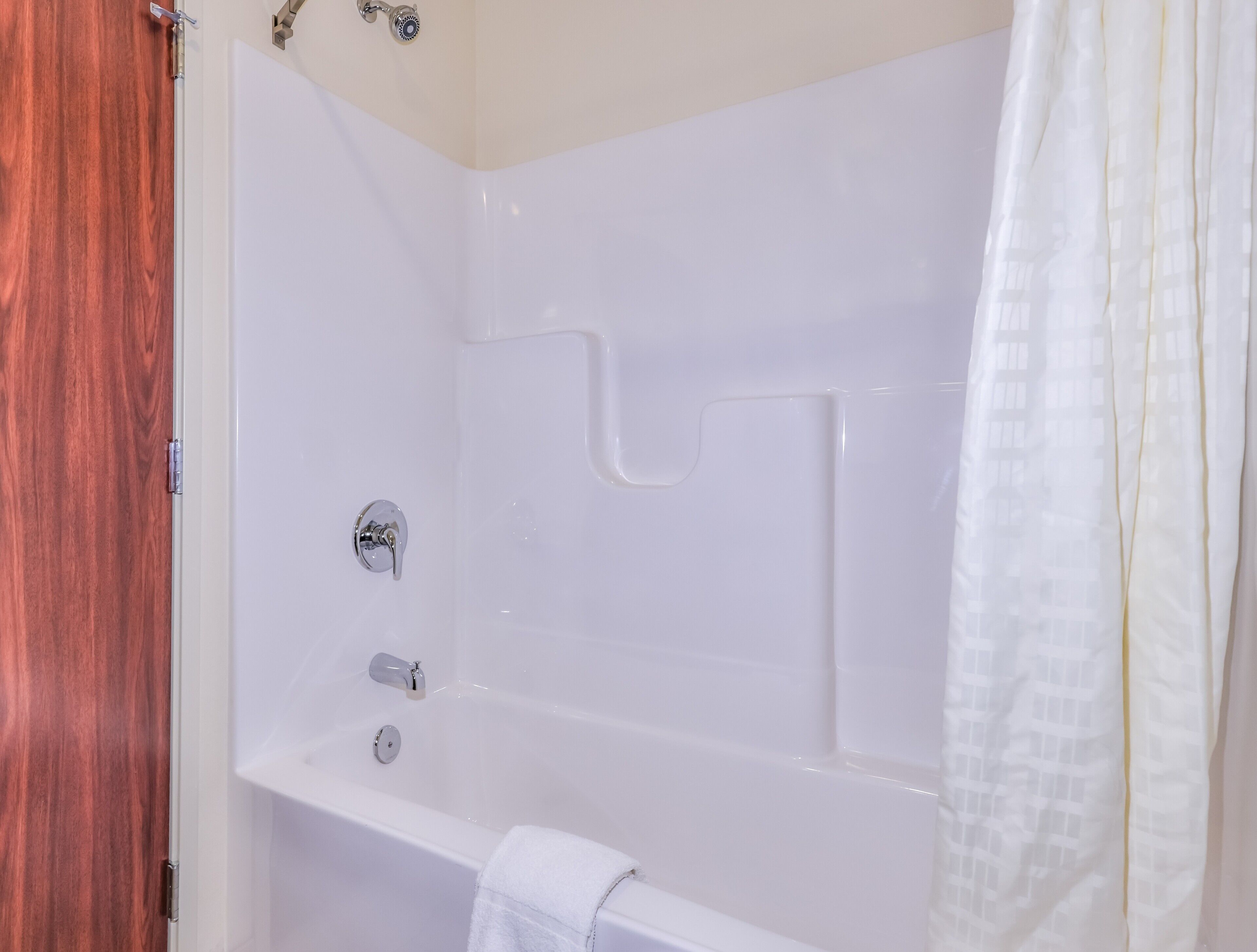Une baignoire blanche avec un rideau de douche, une serviette et une porte en bois.