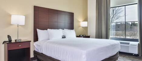 Habitación de hotel con una cama grande, dos mesitas de noche, una lámpara en cada una, una ventana con cortinas y vistas a árboles.