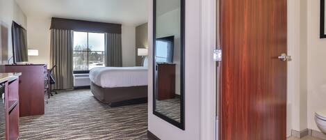 A hotel room with a bed, a desk, a chair, a TV, and a large window with curtains.
