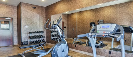 A gym with treadmills, elliptical machines, and a rack of dumbbells.