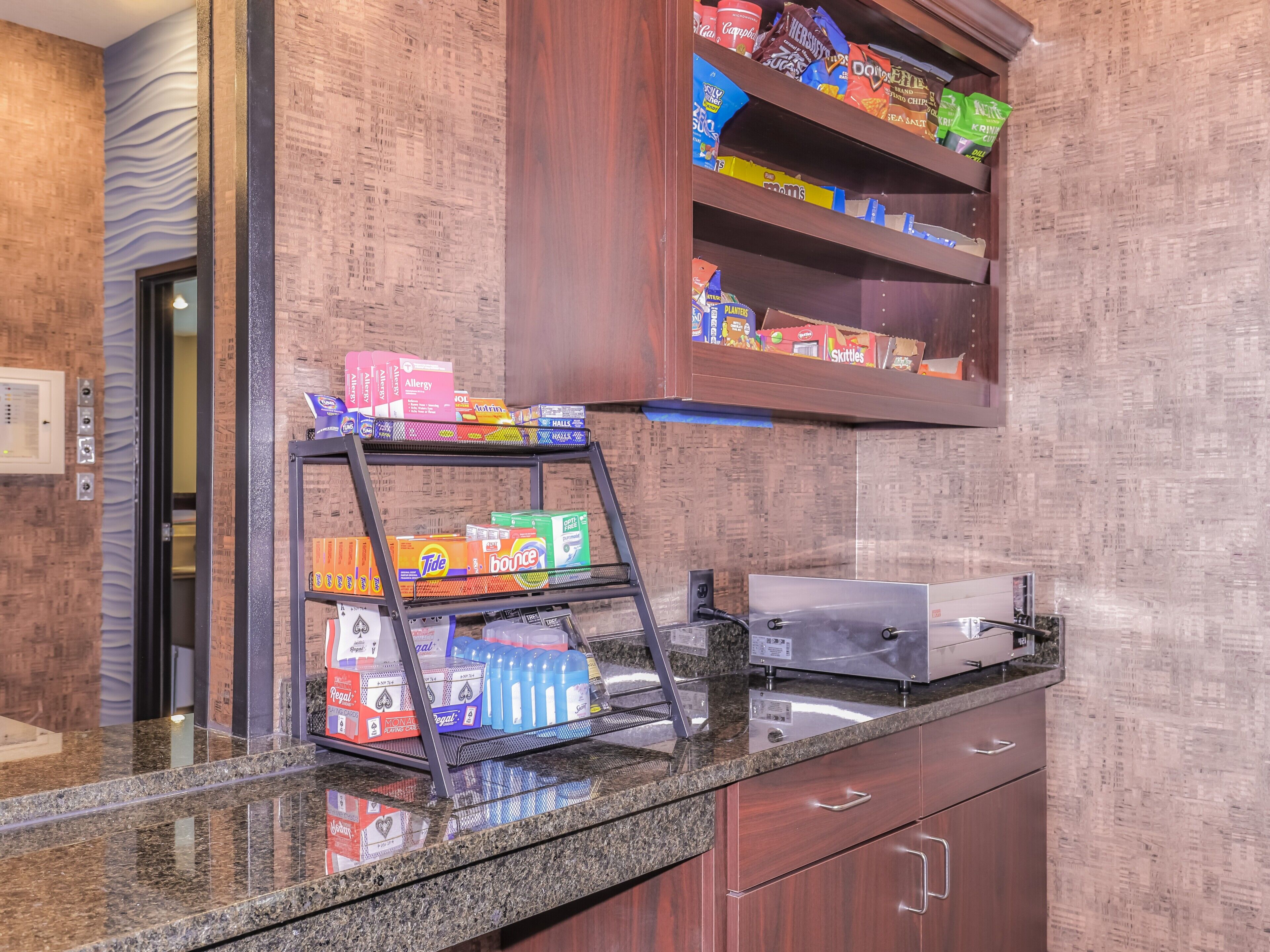 Un angolo cottura in hotel con una macchina da caffè integrata, uno scaffale pieno di snack e un portabevande con diverse bevande.