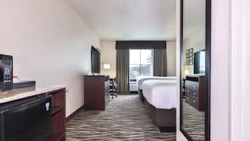 Una habitación de hotel con una cama, un escritorio con un ordenador, un refrigerador y un espejo grande.