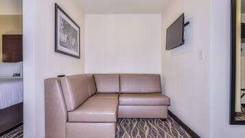 A hotel room with a large L-shaped sectional sofa, a flat-screen TV mounted on the wall, and a patterned carpet.