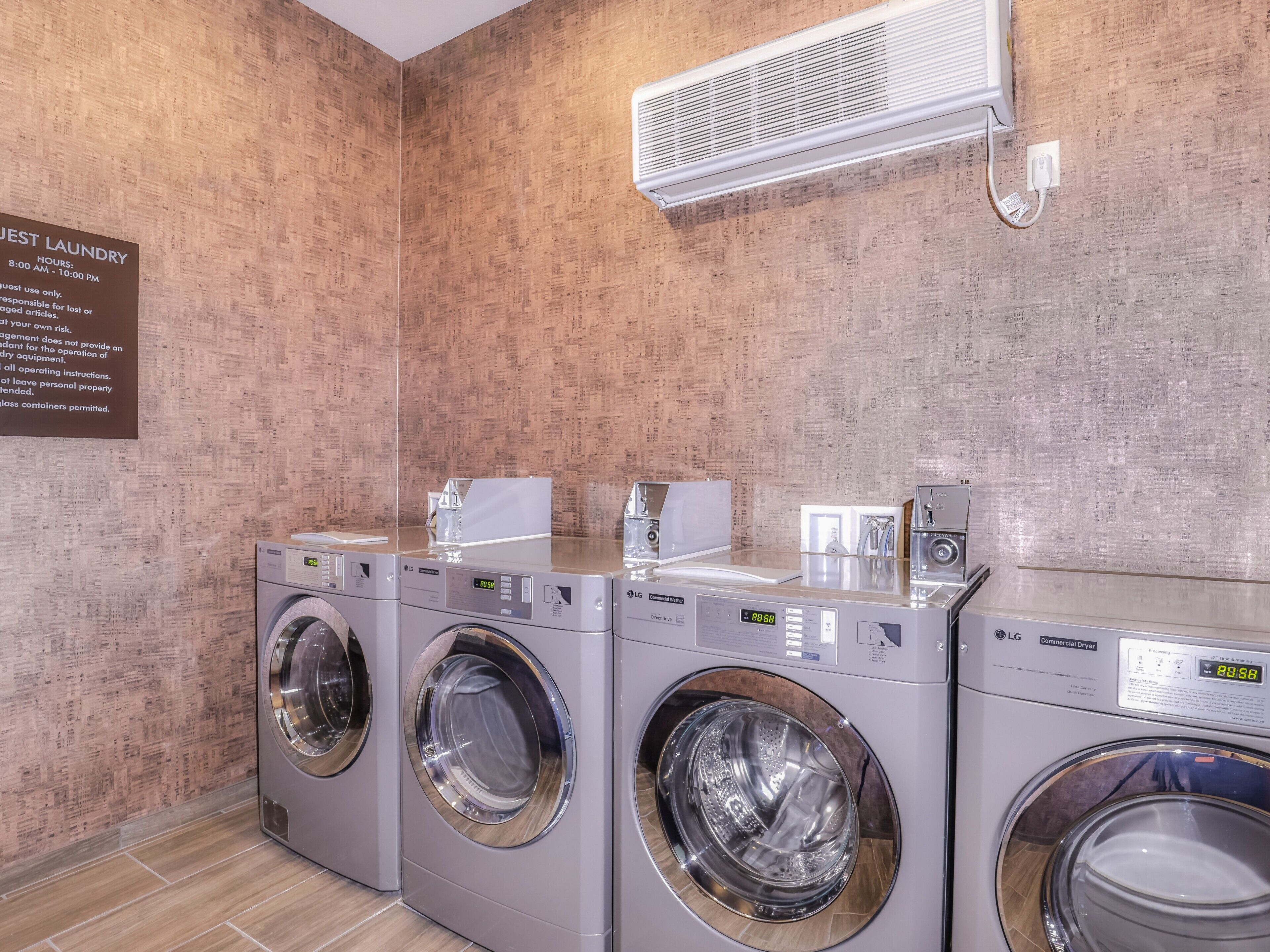 Een wasserette met drie LG wasmachines, een wandairconditioner en een bord met de waszeiten.