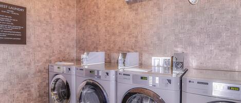 A laundry area with three LG washing machines, a wall-mounted air conditioner, and a sign detailing laundry hours.