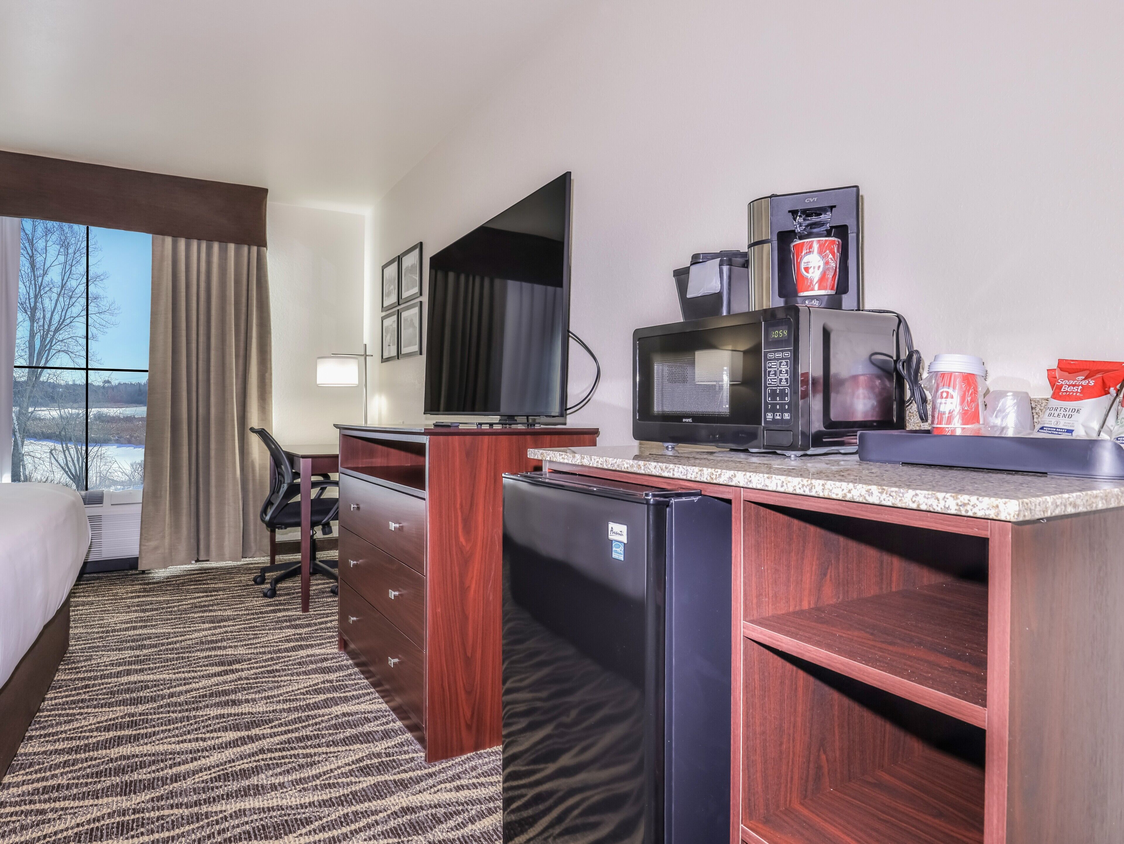 A hotel room with a bed, a desk, a microwave, a coffee maker, and a refrigerator.