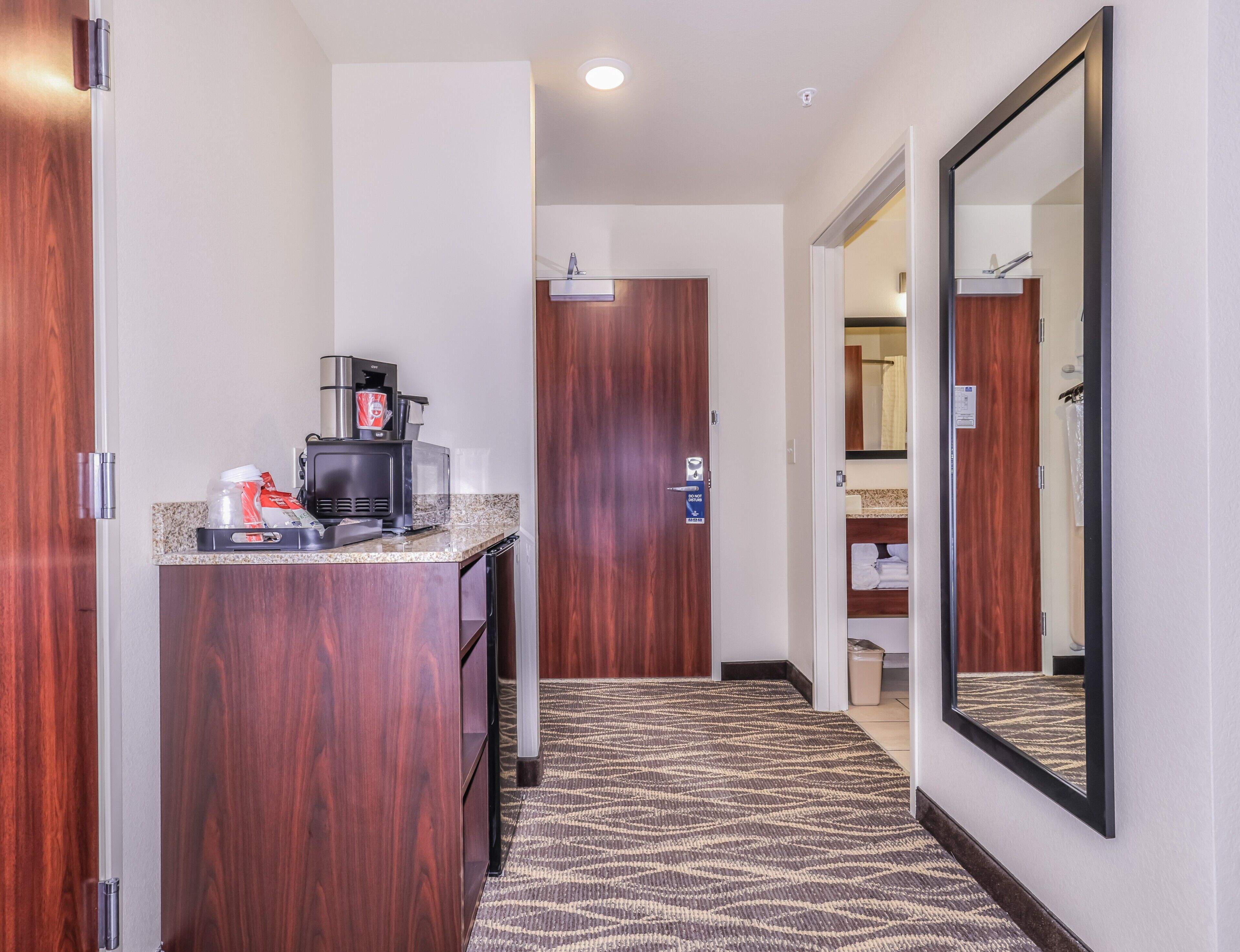 Un couloir d’hôtel avec une kitchenette, un miroir et une porte donnant accès à une salle de bain.