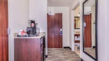 Un couloir d’hôtel avec une kitchenette, un miroir et une porte donnant accès à une salle de bain.