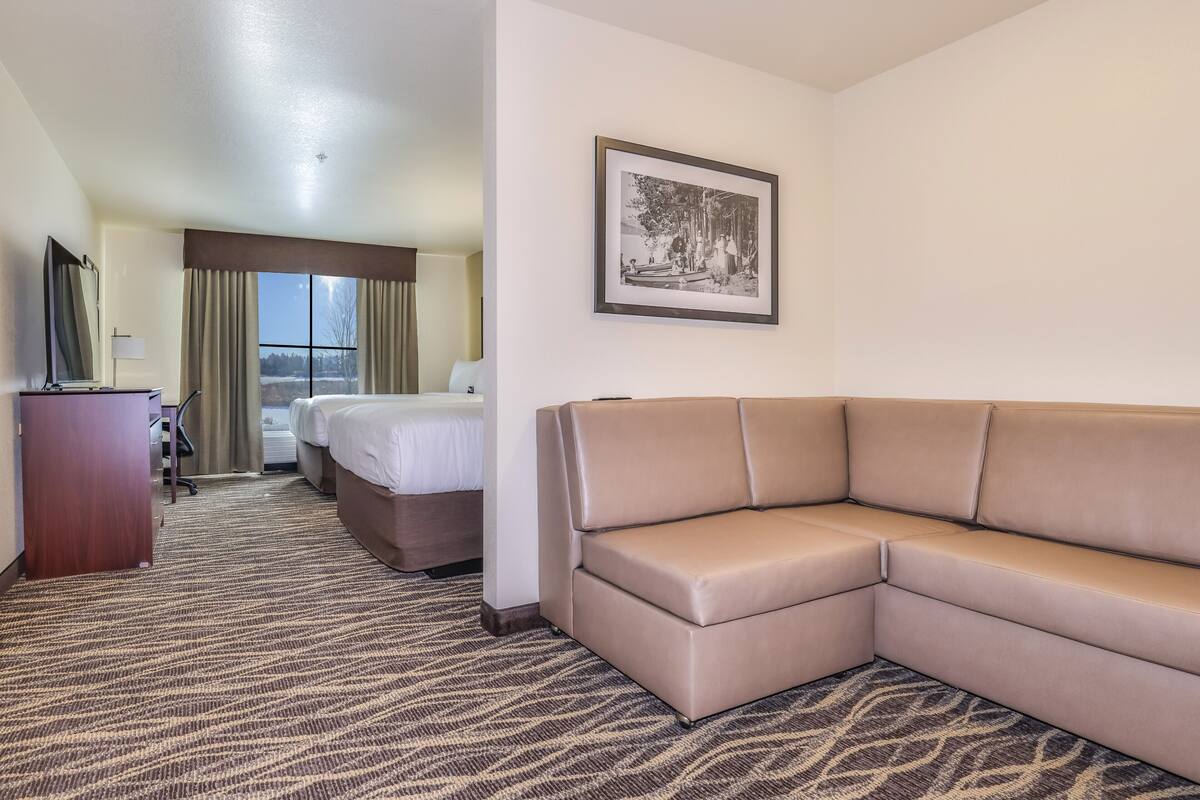 A hotel room with a large bed, a sofa, a desk with a lamp, and a framed picture on the wall.