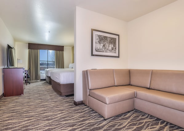 A hotel room with a large bed, a sofa, a desk with a lamp, and a framed picture on the wall.