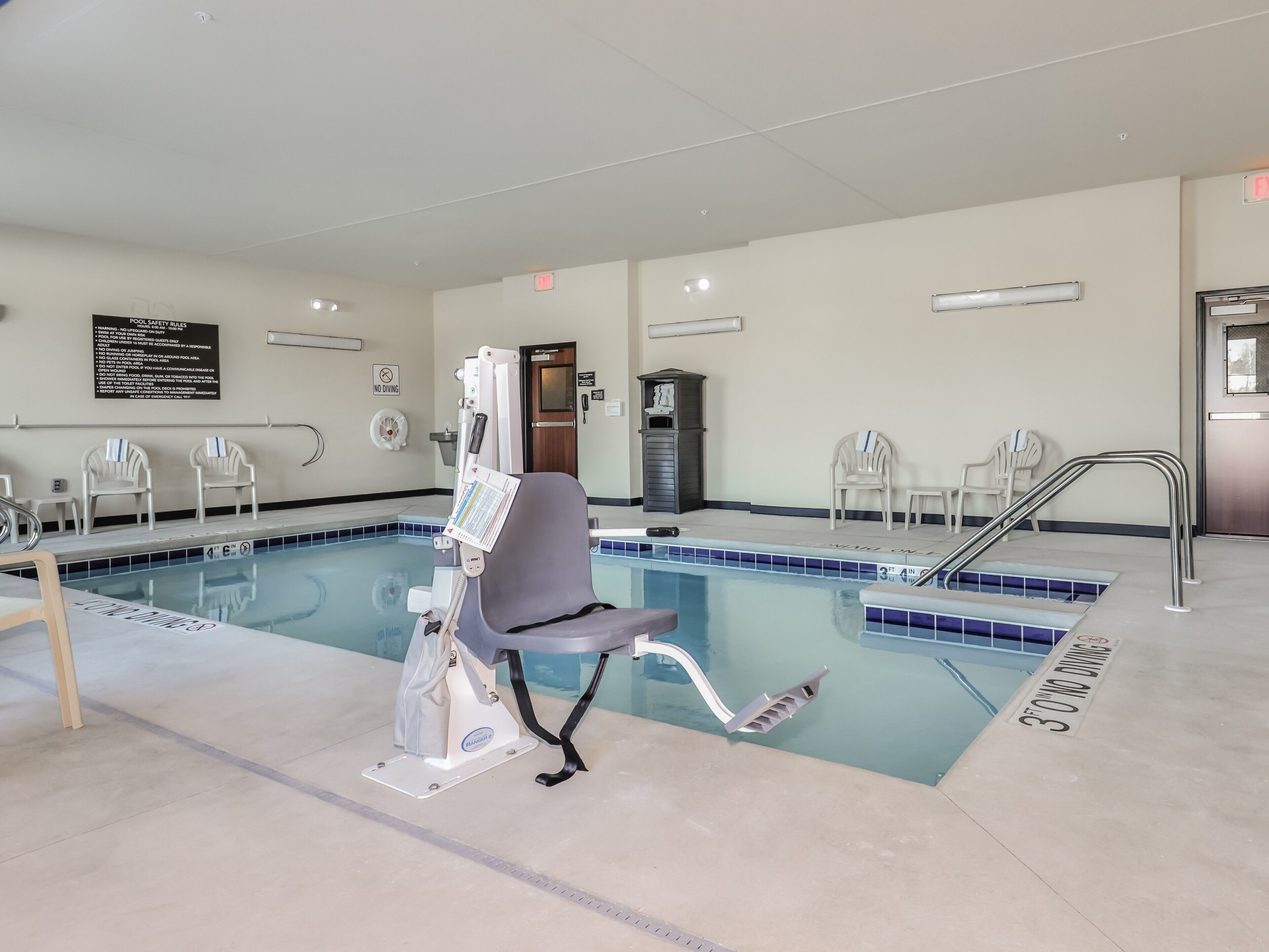 Area piscina con sollevatore per piscine, segnali di sicurezza e cartello che vieta i tuffi.