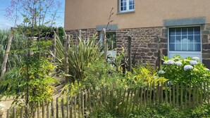 Una casa con fachada de piedra, cerca de madera y diversas plantas y flores.