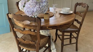 Una mesa de madera con sillas, un jarrón de flores y una taza con platillo.