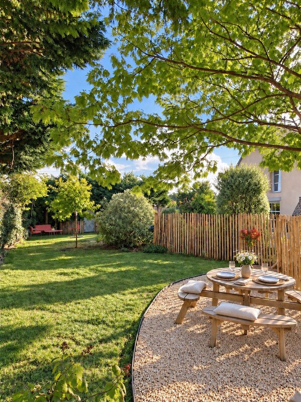 Un giardino curato con un tavolo e sedie in legno, circondato da una recinzione di legno e diverse piante.