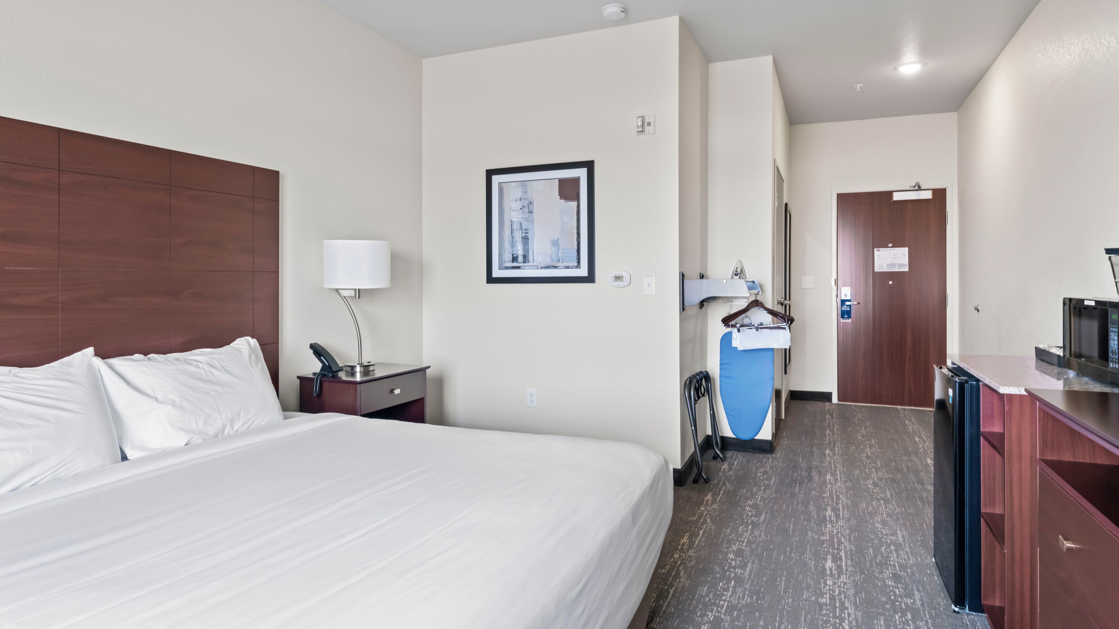 A hotel room with a large bed, a desk with a lamp, a framed picture on the wall, and a microwave on the counter.