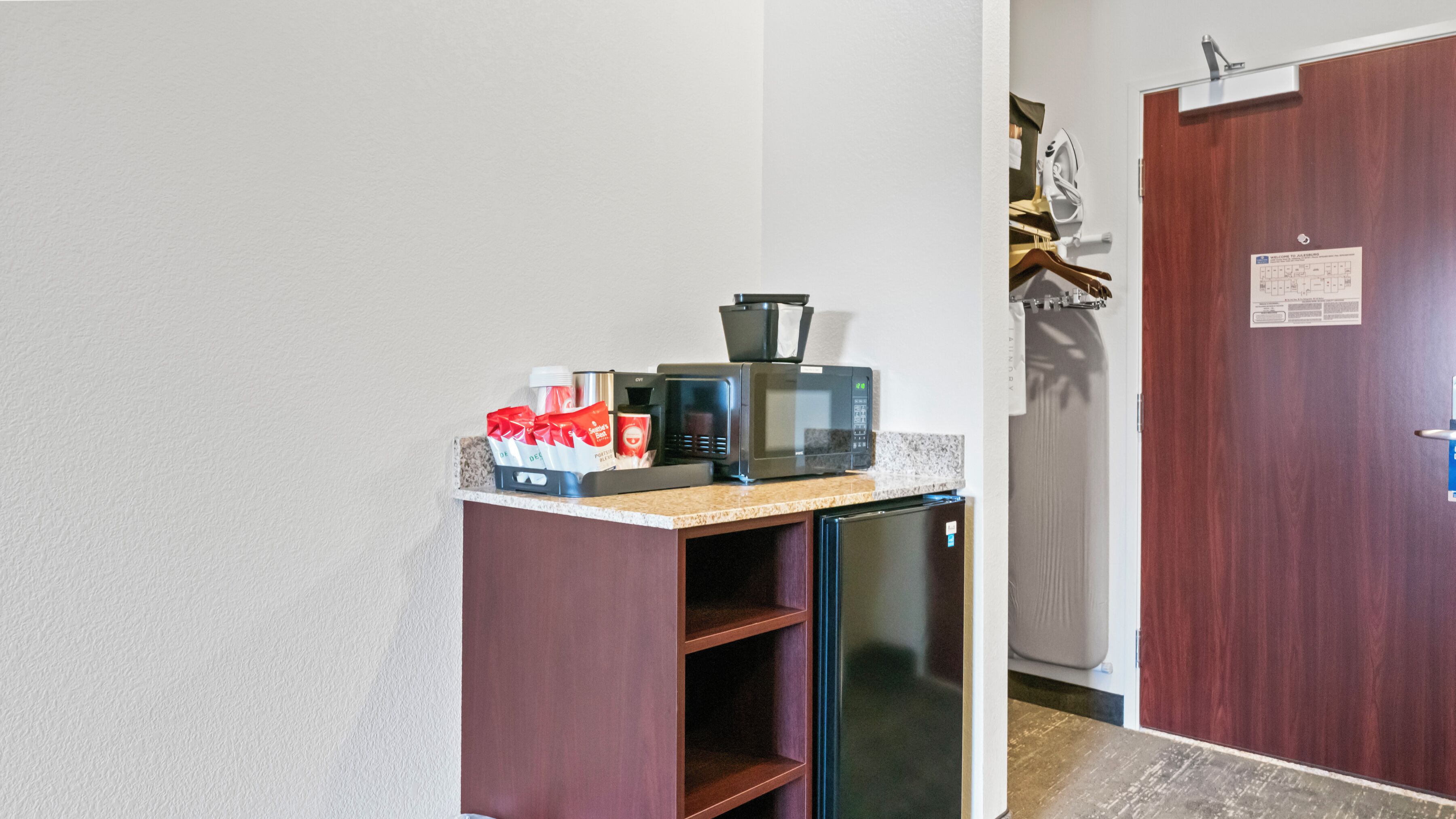 Una kitchenette equipada con microondas, tostadora y cafetera. Se observa una puerta con un cartel.