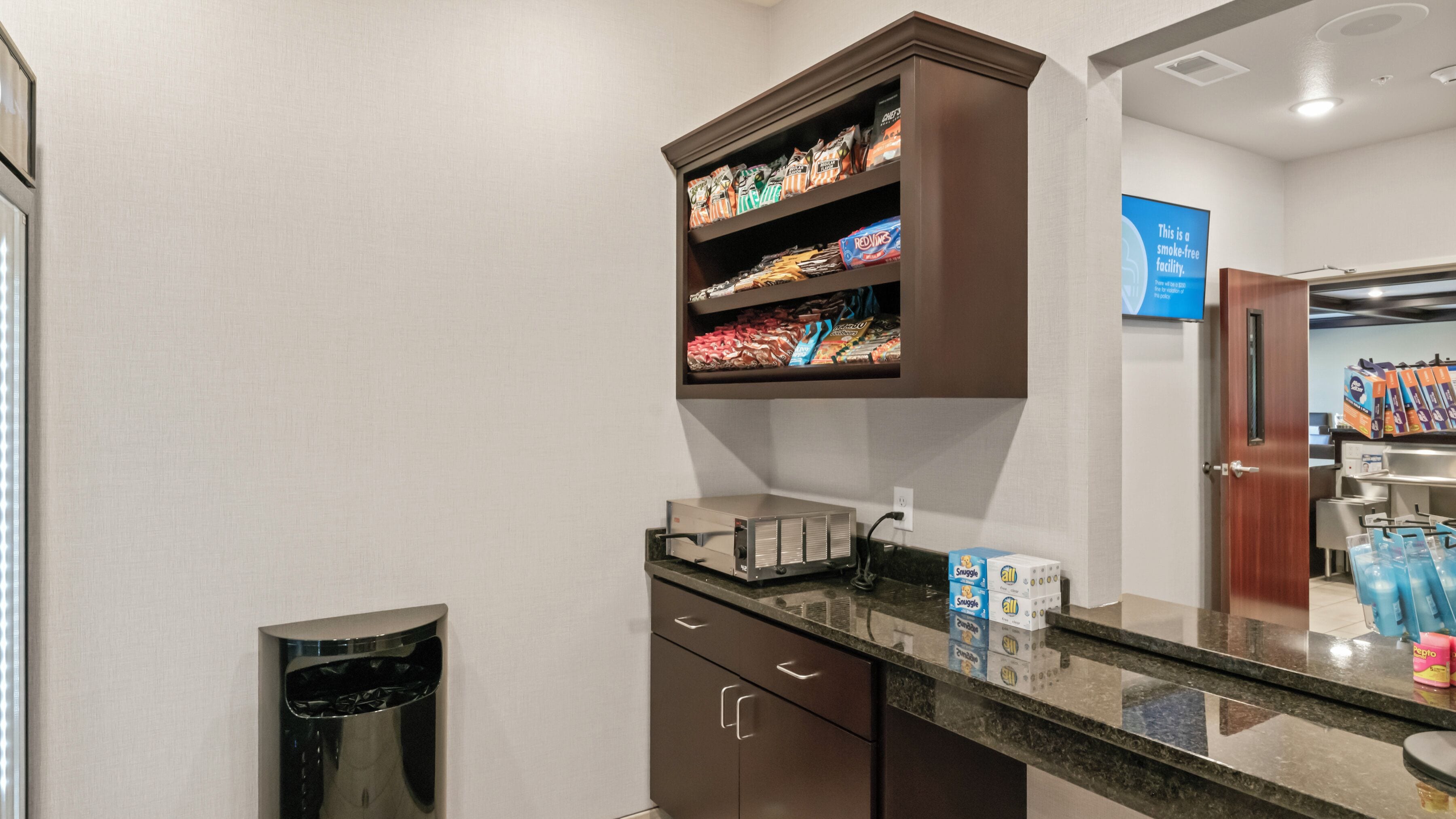 Een hotelbadkamer met een wastafel, een prullenbak, een plank met toiletartikelen en een bordje waarop staat dat het een rookvrije accommodatie is.