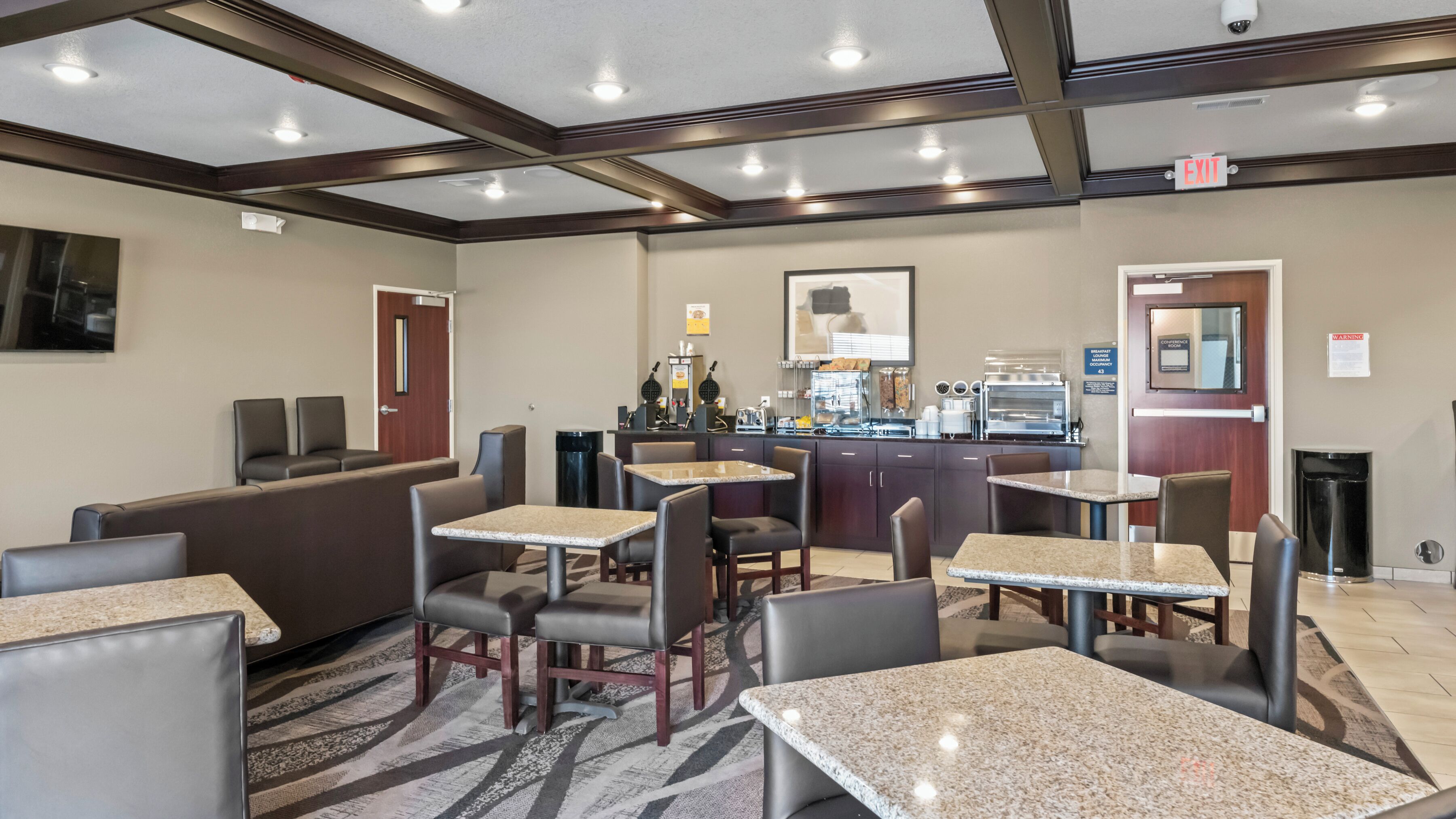 A hotel lobby with seating areas, a counter with food items, and a visible exit sign.