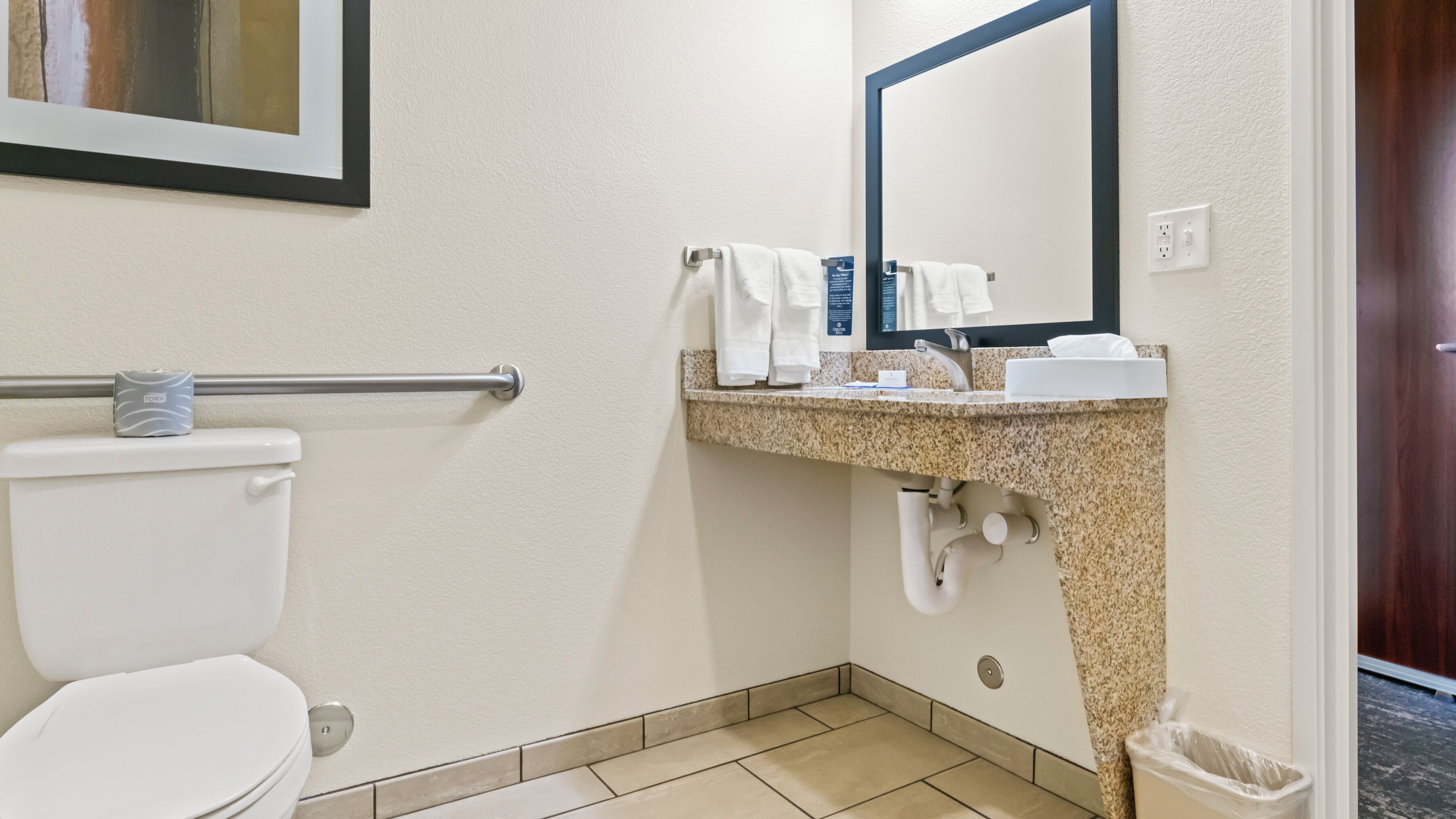 A standard hotel bathroom with a toilet, a sink with a mirror, and a towel rack.