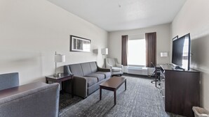 Een hotelkamer met een bank, fauteuil, salontafel, televisie en een bureau met een computer.