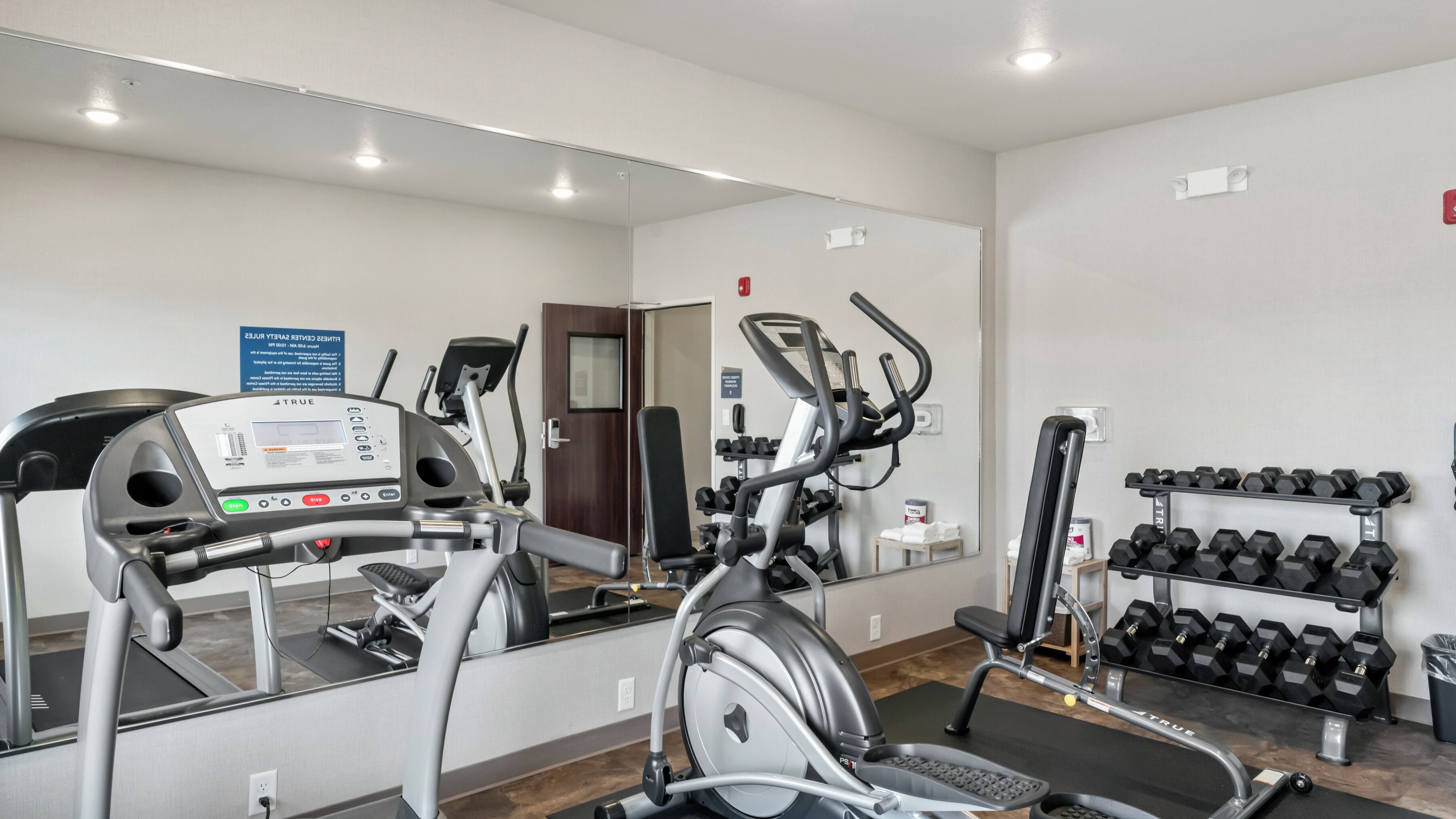 Un gimnasio con equipo de cardio, máquinas de pesas y mancuernas.