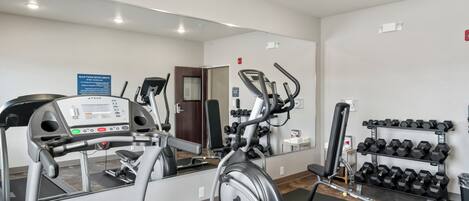 Un gimnasio con equipo de cardio, máquinas de pesas y mancuernas.