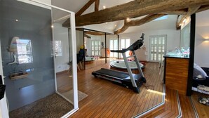 A spacious room with a wooden floor, a treadmill, a glass shower enclosure, and a large window. - Hôtel Particulier Hyper Centre de Rochefort (Rochefort)