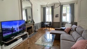 A living room with a flat-screen TV, a glass coffee table, a grey sofa, and a fireplace. - Hôtel Particulier Hyper Centre de Rochefort (Rochefort)