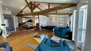 A spacious living room with a high ceiling supported by exposed wooden beams, a sofa, a coffee table, and a view of a balcony. - Hôtel Particulier Hyper Centre de Rochefort (Rochefort)