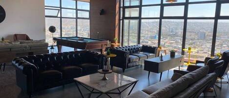 A spacious living area with leather sofas, a pool table, and large windows offering a city view.