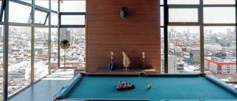 A pool table in a room with large windows, a wooden ceiling, and patterned floor tiles.