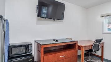 Una habitación pequeña con un escritorio de madera, una silla, un televisor fijado a la pared y un microondas en el suelo.