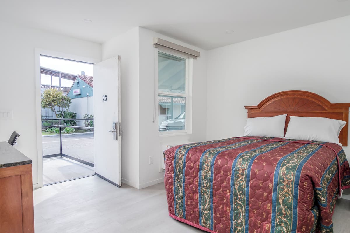 Habitación de hotel con cama, cabecero de madera y ventana con vista a la calle.