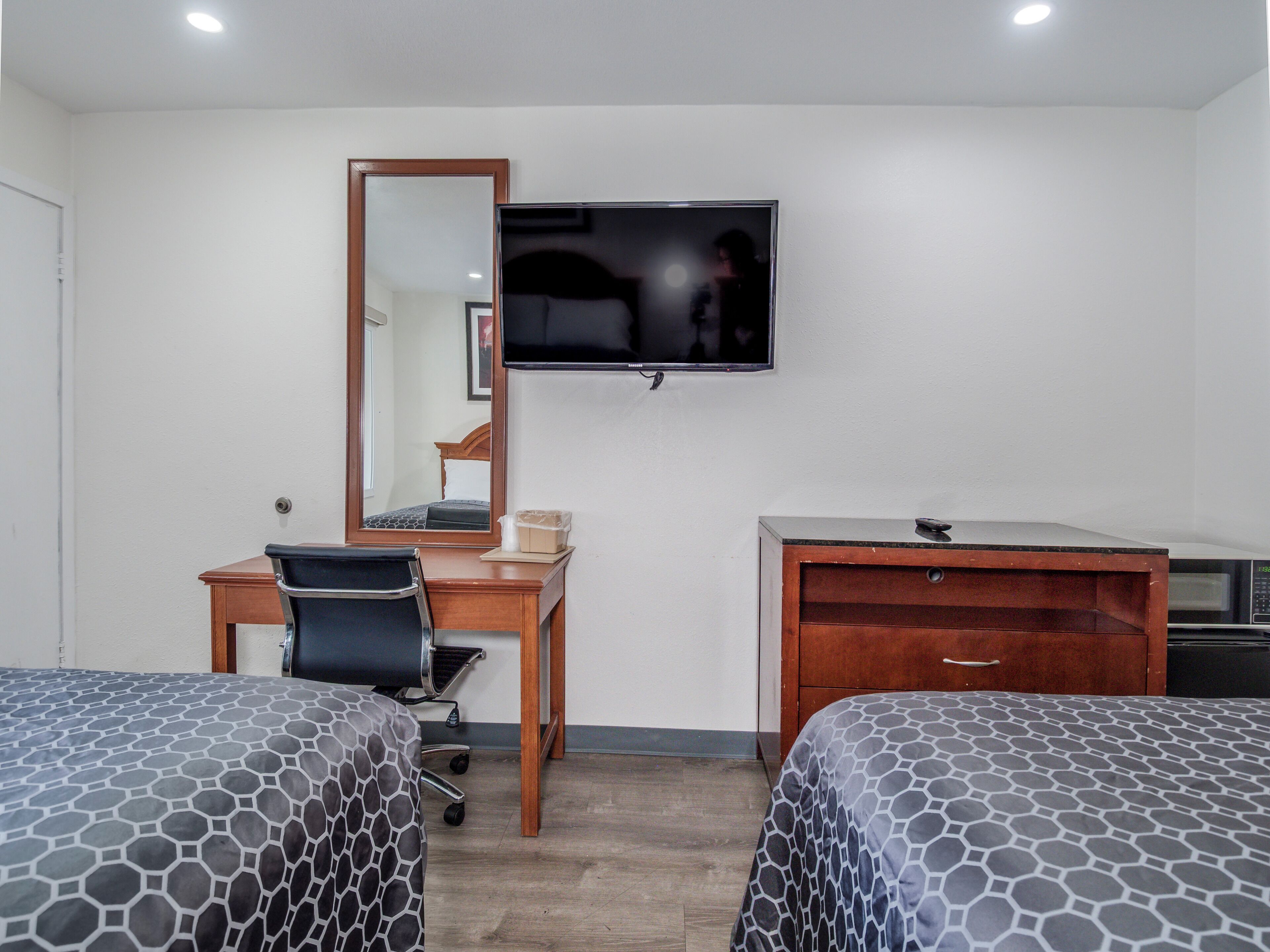 Una habitación de hotel con dos camas, un escritorio, una silla, un televisor, un espejo y un aparador de madera.